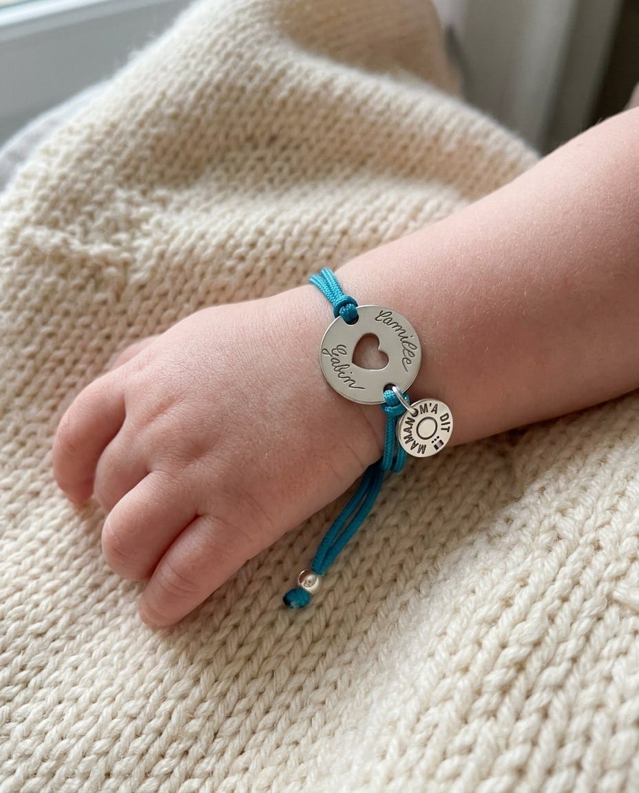 Poignet de bébé avec un bracelet cordon turquoise et une médaille cœur